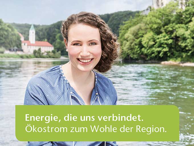 Eine Frau sitzt auf einem Boot und lächelt in die Kamera. Auf dem Bild steht der Text "Energie, die uns verbindet. Ökostrom zum Wohle der Region".