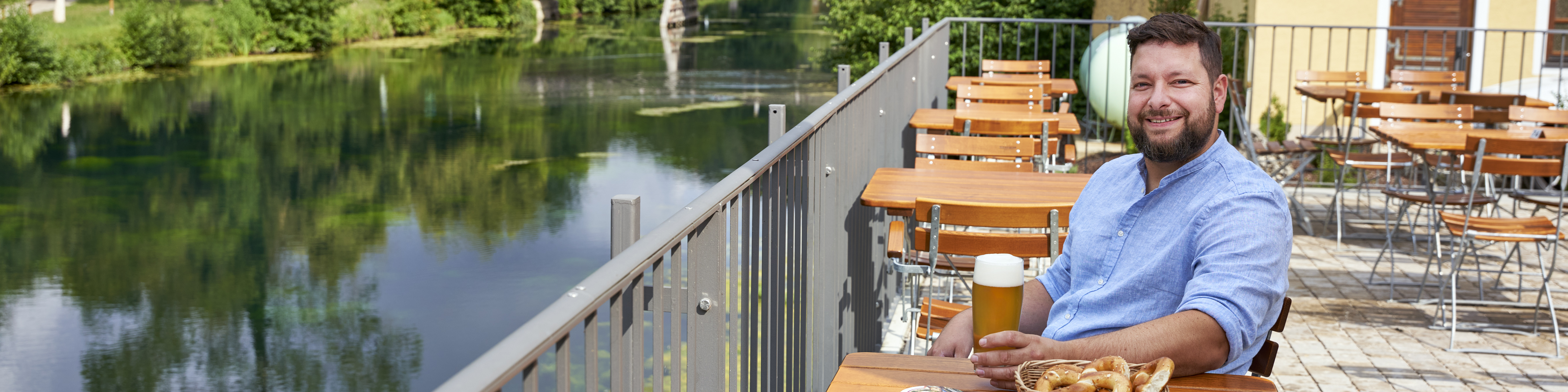 Ein Mann sitzt mit Bier und Brezen in einem Biergarten an einem Fluss